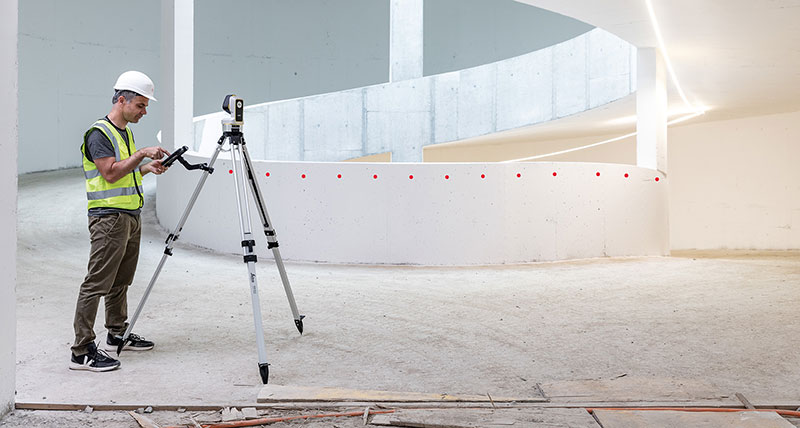 Leica iCON iCS20 motorised construction tool used by worker high-vis vest to measure a curved concrete wall.